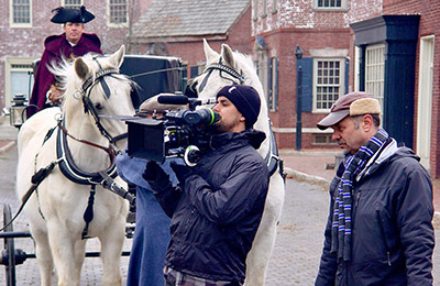 A man is filming two horses in the street.