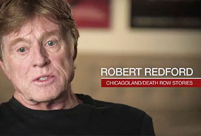 A man in black shirt sitting down next to red wall.