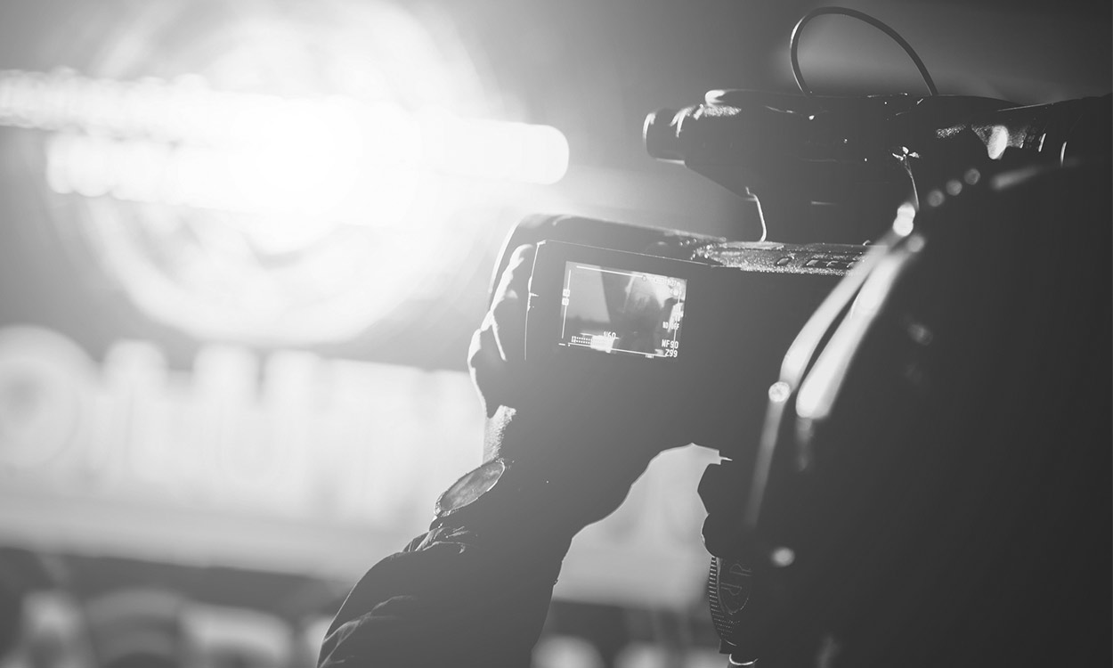 A person holding up a video camera in front of a car.